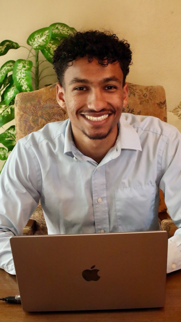 Elijah Harris smiling at his desk with a laptop